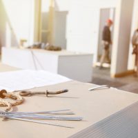 Building plan, eye bolt and screws on plasterboard panels with workers in background